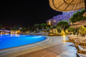 a swimming pool at night with a hotel in the background at Olbios Marina Resort Hotel in Kumkuyu