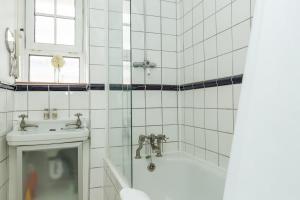 uma casa de banho em azulejos brancos com uma banheira e um lavatório. em Lovely 2 Bedroom Apartment in Waterloo em Londres