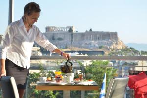 una mujer parada en un balcón con una mesa con comida en Acropolis Ami Boutique Hotel, en Atenas