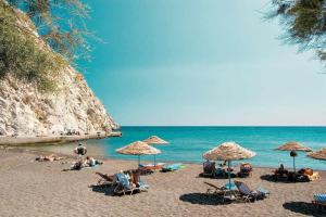 un gruppo di persone seduti su una spiaggia con ombrelloni di Santorini Seaside Retreat - Flora's Summer Escape a Perissa