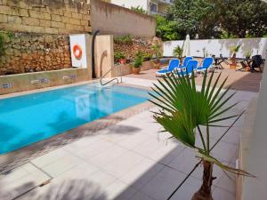 a swimming pool with blue chairs and a palm tree at 2Bed flat w shared heated pool in MLH by Homely! in Mellieħa