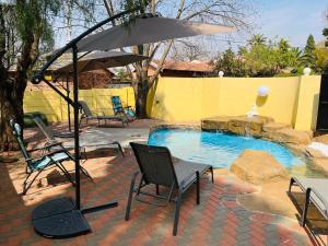 un patio con sillas y una sombrilla junto a la piscina en Khubonye Royal Guesthouse, en Randjesfontein