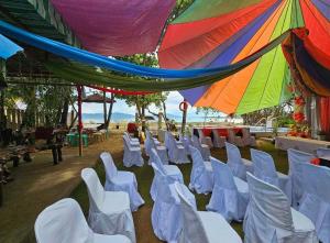 grupa białych krzeseł pod kolorowym parasolem w obiekcie Camp Wadi Codial Beach Resort w mieście San Pedro