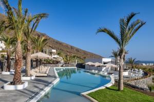 a pool with palm trees and umbrellas at a resort at Palm Island Suites in Imerovigli