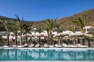 a swimming pool with umbrellas and chairs and palm trees at Palm Island Suites in Imerovigli