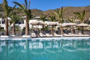 a swimming pool with chairs and umbrellas and palm trees at Palm Island Suites in Imerovigli