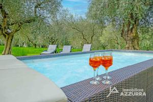 two wine glasses sitting on a table next to a swimming pool at Villa i Roccoli - Immobiliare Azzurra in Bardolino