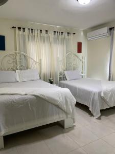 1 Schlafzimmer mit 2 Betten mit weißer Bettwäsche und Vorhängen in der Unterkunft Maria's Entire House HIGUEY 2BD in Higuey