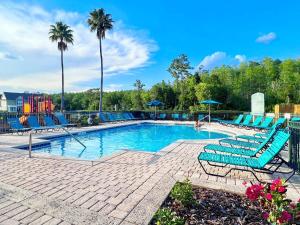 a swimming pool with blue chairs and palm trees at Sunshine Retreat 4 Bed Town Home-4017VBD in Kissimmee