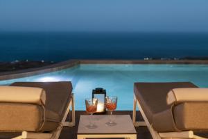 two glasses of wine on a table next to a swimming pool at Almarossa Luxury Villas in Vourvoulos