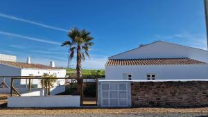a white house with a palm tree and a wall at Milagres de Santa Rita in Vila Nova De Cacela