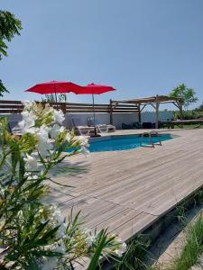 una terraza de madera con 2 sombrillas y una piscina en Mas Constantin en Salin-de-Giraud