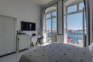 a white bedroom with a bed and a balcony at Skylight - 1873 Seafront Luxury Suites on the Harbor, City Center in Ermoupoli