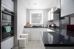 una cocina con armarios blancos y encimeras negras en Deluxe Apartment near Cabot Circus w Parking sleeps 5 en Bristol