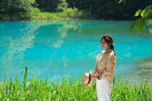 Eine Frau, die vor einem blauen See steht. in der Unterkunft Urabandai Lake Resort Geihinkan Nekoma Rikyu in Kitashiobara