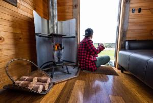 a person sitting on the floor in front of a stove at Altitude - A Tiny House Experience in a Goat Farm in Romsey