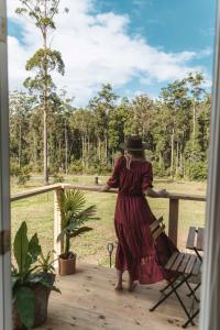 una mujer con un vestido y sombrero de pie en un porche en Kookaburra Cabin en Palmwoods