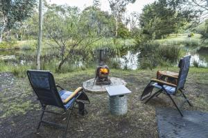 two chairs and a fire pit next to a pond at Tiny Hideaway at Cloverhills in Newham