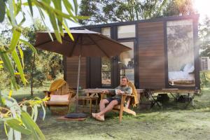 a woman sitting at a table in front of a tiny house at Womburra Vineyard Tiny Stay 