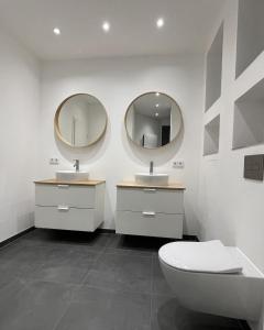 a bathroom with two sinks and a toilet and mirrors at Stadtjuwel: Zentral & Modern in Lichtenfels