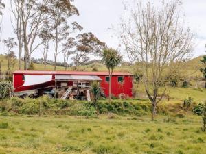 a red barn in the middle of a field at Streamside Tiny House in Mangatarata