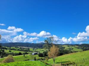 een groene heuvel met een boerderij in de verte bij Deloraine Tiny Retreat in Whangarei