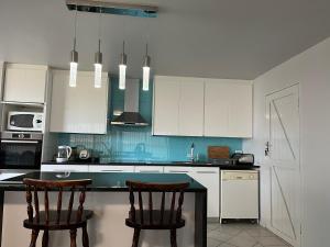 a kitchen with white cabinets and two bar chairs at By The Beach - Beachfront Apartment & Home in Langebaan