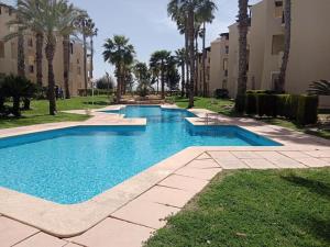 a large swimming pool with palm trees and buildings at El Oasis de Roda Golf Apartment in San Javier