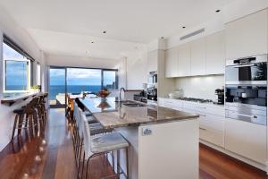 a kitchen with white cabinets and a large island with bar stools at Curley Sunrise - Oceanfront in Curl Curl