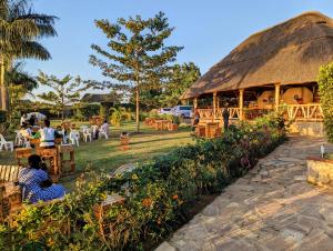 a restaurant with a thatched roof with people sitting at tables at Oslo Gardens Bed & Breakfast in Entebbe