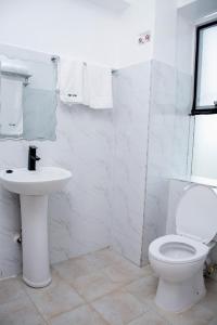 Baño blanco con aseo y lavamanos en The Grand Rocks Hotel Limited, en Eldoret