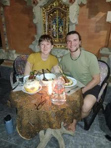 Um homem e uma mulher sentados à mesa com comida. em Wikan House em Bebandem