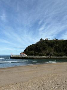 a beach with a pier and a house on a hill at Apartamento Arena in Ribadesella