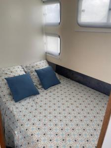 a bed with two blue pillows in a small room at BATEAU - CANAL DU NIVERNAIS NIEVRE in Bazolles
