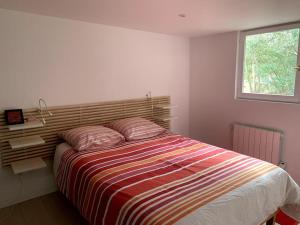 a bedroom with a bed with a striped comforter and a window at Maison familiale - Marina de Talaris - Lac Lacanau in Lacanau