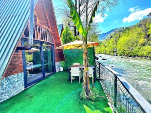 a balcony with a table and an umbrella next to a river at Tabiat Bungalows in Çamlıhemşin
