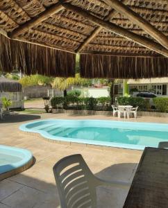 - une piscine avec un parasol en paille, une table et des chaises dans l'établissement Pousada Arco Iris Ilhéus, à Ilhéus