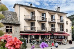 um edifício com pessoas sentadas em mesas à frente dele em Logis Hotel Restaurant Du Commerce em La Canourgue