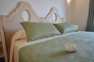 Una cama con dos almohadas verdes y un sombrero. en Le Anfore Hotel, en Villasimius