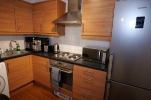 La cuisine est équipée d'armoires en bois et d'un réfrigérateur en acier inoxydable. dans l'établissement Cozy Haven Flat, à Milton Keynes