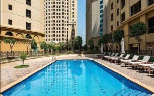 a large swimming pool with lounge chairs and buildings at Stylish and Sleek: Modern Well-Furnished One Bedroom Hall and Kitchen Apartment in Dubai