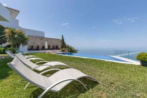 a row of white lawn chairs sitting next to a swimming pool at Casa Villa Lumar in Almuñécar