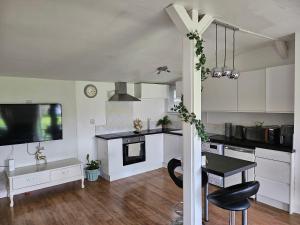 cocina con armarios blancos, mesa y TV en Remarkable 1-Bed Cabin in Dunmow, en Great Dunmow