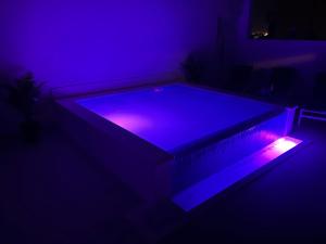 Apartment Marinely في قشتيلا: غرفة مظلمة مع حمام سباحة مع أضواء أرجوانية