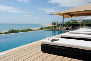 a swimming pool with chaise lounges and the ocean at Eco Beach Wilderness Retreat in Broome