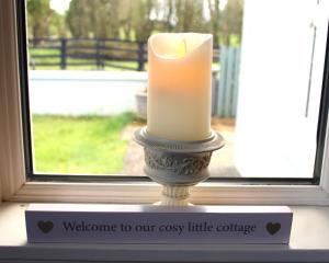 una candela seduta sul davanzale di una finestra di fronte a una finestra di Heather Cottage and Shepherds Hut a Knock