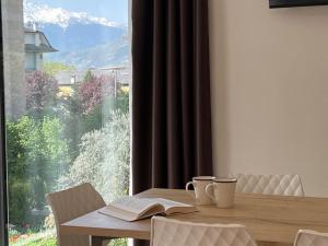 a table with two cups and a book and a window at Bernina Suites - 150 metres to Bernina Express in Tirano