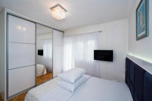 a white bedroom with a bed and a mirror at M&M Pelivan apartment in Kaštela