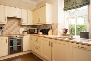 cocina con armarios blancos, fregadero y ventana en Pentland Cottage, en Norham
