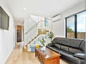 a living room with a black leather couch and a table at Gorgeous Three Bedroom Home with Free Parking in Auckland